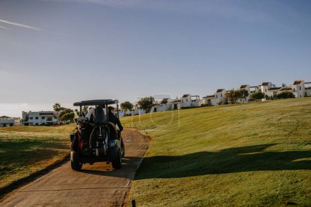 Téléchargez les photos : Sotogrande, Espagne - 23 janvier 2024 - Un golfeur conduisant une voiturette de golf sur un sentier sur un terrain de golf avec des bâtiments résidentiels en arrière-plan sous un ciel bleu clair. - en image libre de droit
