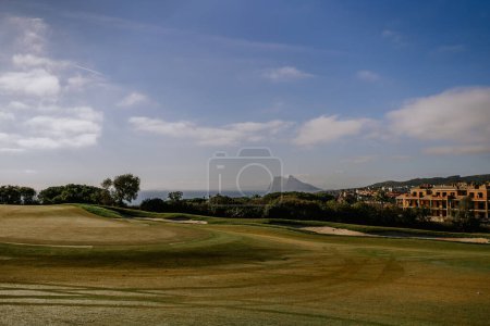 Foto de Sotogrande, España - 23 de enero de 2024 - Campo de golf con calles segadas, una vista del Peñón de Gibraltar a lo lejos, cielos despejados y paisajes costeros. - Imagen libre de derechos