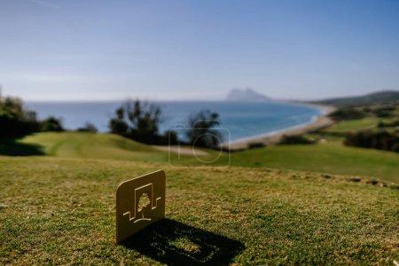 Foto de Sotogrande, España - 23 de enero de 2024 - Un marcador de camiseta de golf en primer plano con una vista panorámica borrosa de la costa y Gibraltar en el fondo. - Imagen libre de derechos