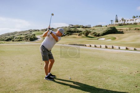 Sotogrande, España - 23 de enero de 2024 - Un golfista con camisa a rayas y gorra en medio de un campo de golf con colinas verdes y un cielo despejado al fondo.