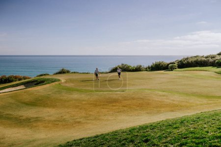 Téléchargez les photos : Sotogrande, Espagne - Janvier, 23, 2024 - Deux golfeurs sur un vert avec l'océan en arrière-plan, un ciel clair au-dessus, et des informations de dossier visibles dans la superposition. - en image libre de droit