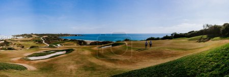 Téléchargez les photos : Sotogrande, Espagne - 23 janvier 2024 - Vue panoramique d'un terrain de golf avec des golfeurs, des pièges à sable et une vue dégagée sur la mer et le littoral sous un ciel bleu. - en image libre de droit