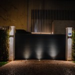 Sotogrande, Spain - January, 23, 2024 - A night view of a luxury home's entrance with a black sliding gate, white walls, and soft lighting.