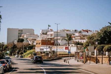 Photo for Santa Margarita, Spain - January 24, 2024 - sunny street scene with cars, palm trees, and Mediterranean-style buildings under a clear blue sky. - Royalty Free Image