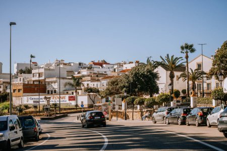 Photo for Santa Margarita, Spain - January 24, 2024 - sunny street scene with cars, palm trees, and Mediterranean-style buildings under a clear blue sky. - Royalty Free Image
