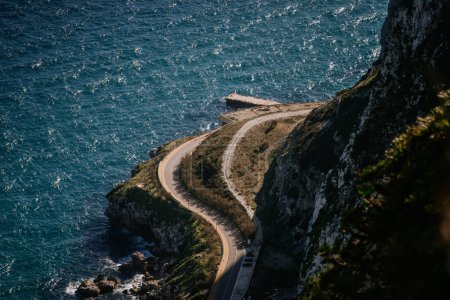 Foto de Gibraltar, Gran Bretaña - 24 de enero de 2024 - Un sinuoso camino costero junto a un acantilado empinado y el mar azul. - Imagen libre de derechos