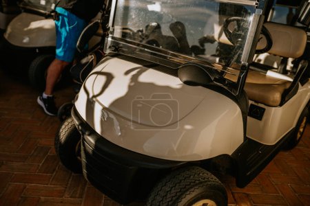 Sotogrante, Spanien - 25. Januar 2024 - Nahaufnahme der Front eines Golfwagens mit Schatten, die sich auf seiner glänzenden Oberfläche spiegeln, daneben das Bein einer Person.