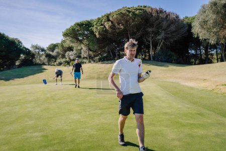 Foto de Sotogrante, España - 25 de enero de 2024 - Dos golfistas están caminando en el campo, uno en primer plano sosteniendo un club y el otro en el fondo. - Imagen libre de derechos