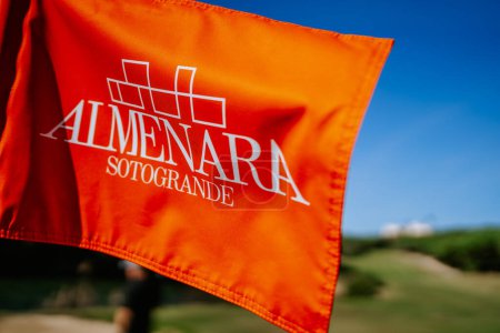 Téléchargez les photos : Sotogrante, Espagne - 25 janvier 2024 - Un drapeau orange avec le logo "ALMENARA SOTOGRANDE" sur un terrain de golf, ciel bleu en arrière-plan. - en image libre de droit