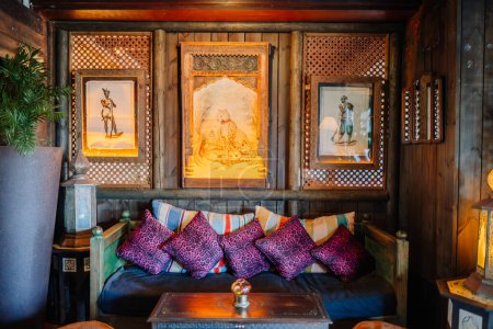 Sotogrante, Spain - January 25, 2024 - An exotic lounge with colorful cushions, wood paneling, and artwork within intricately carved frames, highlighted by warm lighting.