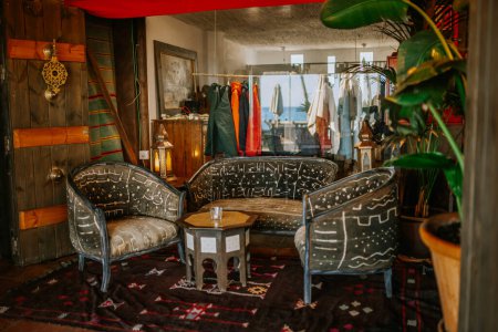 Sotogrante, Spain - January 25, 2024 - Eclectic lounge with patterned sofas, ornate rugs, wooden walls, reflective glass, green plants, and a hanging garment rack.