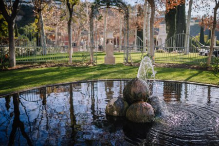 Téléchargez les photos : Sotogrante, Espagne - 26 janvier 2024 - fontaine d'eau avec des pierres sphériques dans un étang réfléchissant, une pelouse soignée, des arbres et un jardin clos en arrière-plan. - en image libre de droit