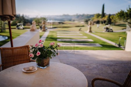Téléchargez les photos : Sotogrante, Espagne - 26 janvier 2024 - table avec un vase de roses roses donnant sur un jardin paysager et un terrain de golf. - en image libre de droit