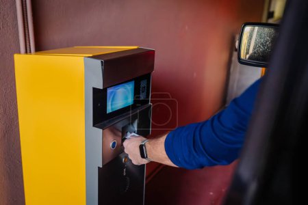 Sotogrante, Spain - January 26, 2024 - person's arm reaching out from a car to use a yellow parking ticket machine.