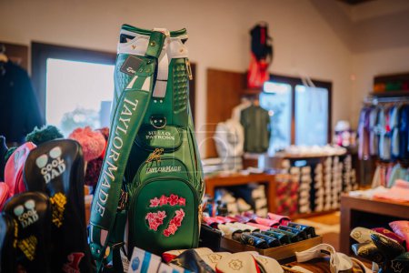 Téléchargez les photos : Sotogrante, Espagne - 27 janvier 2024 - Sac de golf TaylorMade vert avec des fleurs brodées, exposé dans une boutique avec des vêtements et accessoires en arrière-plan. - en image libre de droit