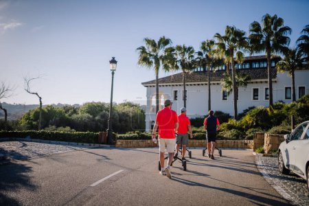 Téléchargez les photos : Sotogrante, Espagne - 27 janvier 2024 - Trois golfeurs marchant sur une route pavée vers un clubhouse entouré de palmiers sous un ciel bleu clair. - en image libre de droit