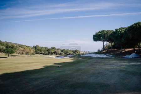 Sotogrante, Spain - January 27, 2024 - Golf course with sand bunkers, trees, and a distant view of an urban area under a sky with wispy clouds.