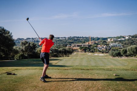 Photo for Sotogrante, Spain - January 27, 2024 - Golfer in follow-through after tee shot on a golf course with clear skies and a backdrop of trees and houses - Royalty Free Image
