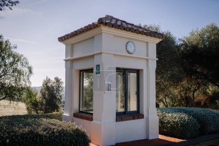 Sotogrante, Spain - January 27, 2024 - Small white building with clock, large windows, tiled roof, surrounded by shrubbery and trees with a clear sky.