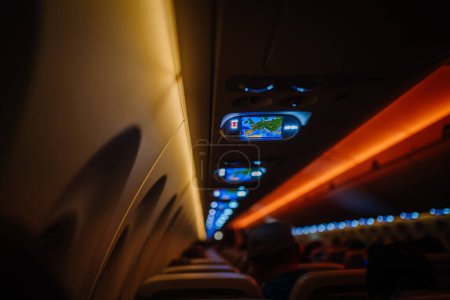 Photo for Riga, Latvia - January 28, 2024 - Airplane cabin interior with dim lighting, overhead monitors displaying map, passengers seated. - Royalty Free Image