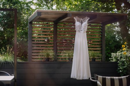 Valmiera, Latvia - July 7, 2023 - Wedding dress hanging on a wooden gazebo with a garden background.