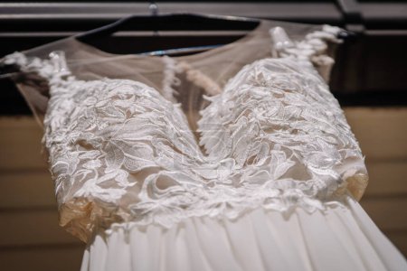 Valmiera, Latvia - July 7, 2023 - Close-up of a white wedding dress with intricate lace detailing on the bodice, hanging against a neutral background.