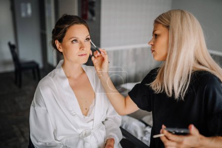 Valmiera, Latvia - July 7, 2023 - A makeup artist is applying makeup to a seated woman in a white robe.