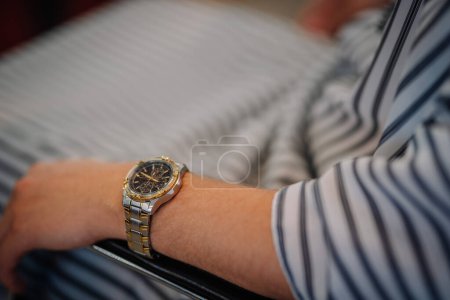 Valmiera, Latvia - July 7, 2023 - Close-up of a man's wrist wearing a gold and silver wristwatch, with a striped barber cape.