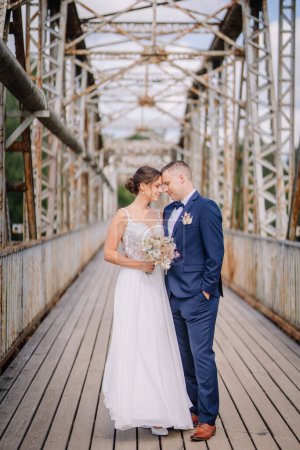 Valmiera, Latvia - July 7, 2023 - A bride and groom affectionately touching foreheads on an old bridge with structural beams above.