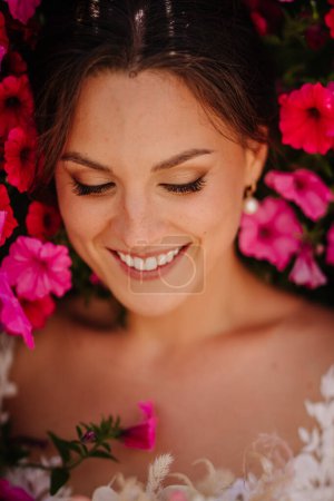 Valmiera, Latvia - July 7, 2023 - Close-up of a smiling bride with eyes closed, surrounded by pink flow