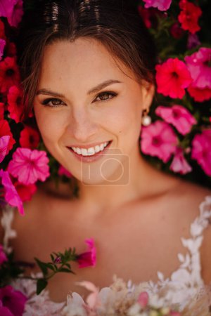 Valmiera, Lettonie - 7 juillet 2023 - Mariée souriante au milieu de fleurs roses vibrantes, robe de mariée visible