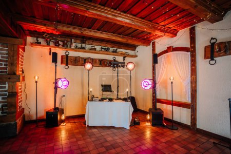 Valmiera, Lettland - 7. Juli 2023 - DJ-Pult mit bunten Bühnenlichtern in einem rustikalen Raum mit Holzbalken und Fliesenboden.