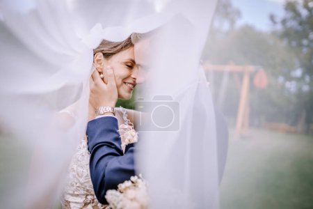 Valmiera, Latvia - July 7, 2023 - Bride and groom intimately close, with the groom's hand on the bride's face under the veil.