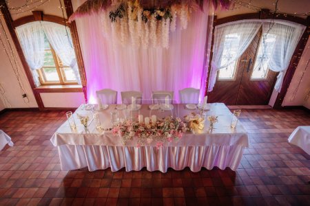 Valmiera, Latvia - July 7, 2023 - Elevated view of a wedding head table with pink lighting and floral decorations.