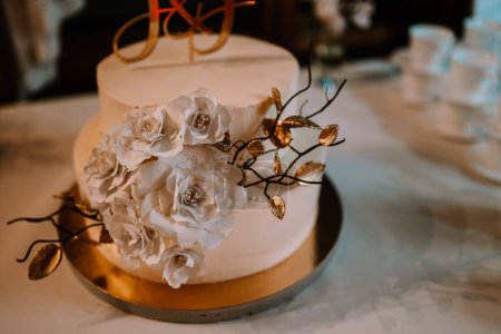 Valmiera, Latvia - July 7, 2023 - Wedding cake with white flowers and golden leaves on a golden base.