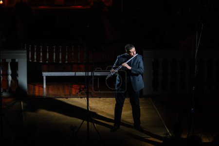 Photo for Valmiera, Latvia - January 7, 2024 - Saint Simon's Church. Solo flutist playing on stage with spotlight, audience in dark, in a church setting with balcony and pillars. - Royalty Free Image