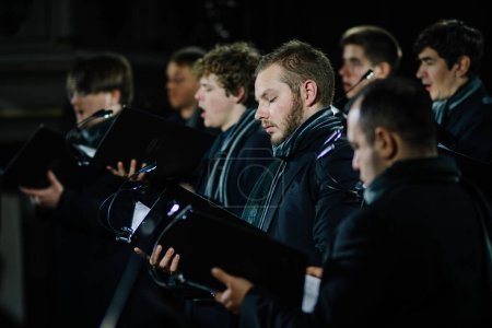 Foto de Valmiera, Letonia - 7 de enero de 2024 - Iglesia de San Simon. Miembros masculinos del coro vestidos de negro con bufandas sosteniendo partituras, enfocados en cantar durante un concierto de la iglesia. - Imagen libre de derechos