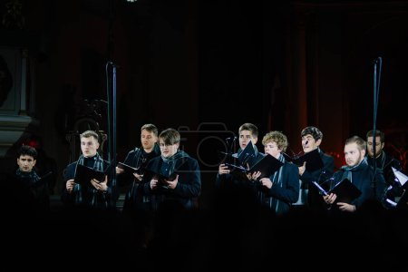 Photo for Valmiera, Latvia - January 7, 2024 - Saint Simon's Church. Male choir singing with sheet music in a church, spotlighted against a dark background with architectural details. - Royalty Free Image
