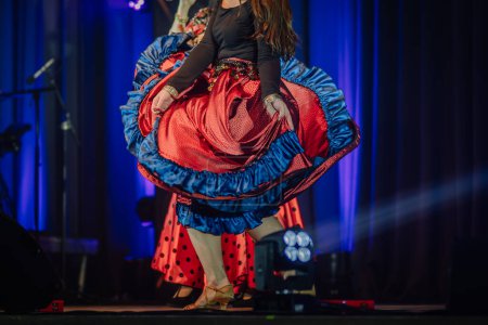 Foto de Valmiera, Letonia - 15 de febrero de 2024 - Un primer plano de una bailarina haciendo girar la falda en un concierto gitano tradicional, con una vibrante iluminación azul en el fondo - Imagen libre de derechos