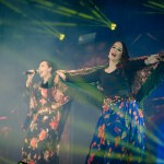 Valmiera, Latvia- February 15, 2024 - Two female performers at a gypsy concert, one singing and the other dancing, both in colorful traditional attire, under green stage lights.