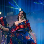 Valmiera, Latvia- February 15, 2024 - A joyful female dancer in a colorful gypsy costume dances under blue stage lights at a concert.