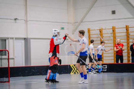 Photo for Valmiera, Latvia - February 17, 2024 -  two floorball players on a court, one in goalie gear giving a thumbs-up to another player, with other players and a coach in the background. - Royalty Free Image