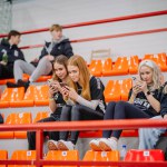 Valmiera, Latvia - February 17, 2024 - spectators in an indoor sports arena. Four young women are seated on orange bleachers, with three of them focused on their smartphones.