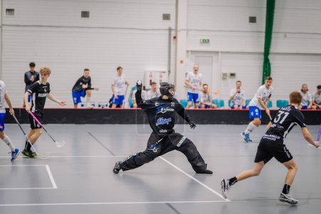 Photo for Valmiera, Latvia - February 17, 2024 - a floorball goalie in a dramatic save stance with players in the background. - Royalty Free Image