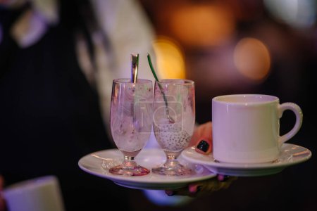 Riga, Latvia - February 16, 2024 - a server's hand holding a tray with two empty glasses that seem to have had a pink dessert and a cup of a hot beverage, possibly tea or coffee.