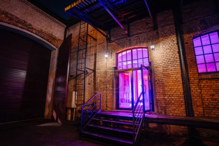 Riga, Latvia - February 16, 2024 - an exterior brick building entrance with a purple-lit doorway and a metal staircase.