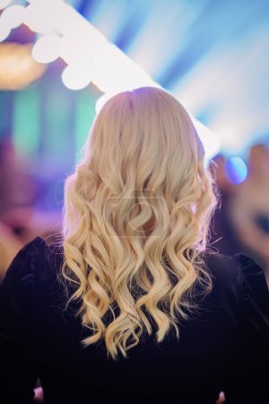 Riga, Lettland - 16. Februar 2024 - Rückansicht einer Person mit langen, lockigen blonden Haaren, vor verschwommenem Hintergrund mit Lichtstrahlen.