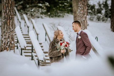 Riga, Latvia - January 20, 2024 - A bride and groom gaze at each other on a snowy path with snow-covered railings and trees around them.