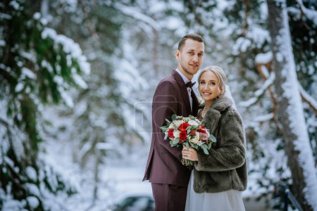 Riga, Latvia - January 20, 2024 - A bride and groom stand together in a snowy forest setting, both looking at the camera.