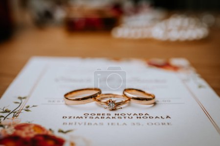 Foto de Riga, Letonia - 20 de enero de 2024 - Dos anillos de boda en un documento con elementos florales en el fondo. - Imagen libre de derechos